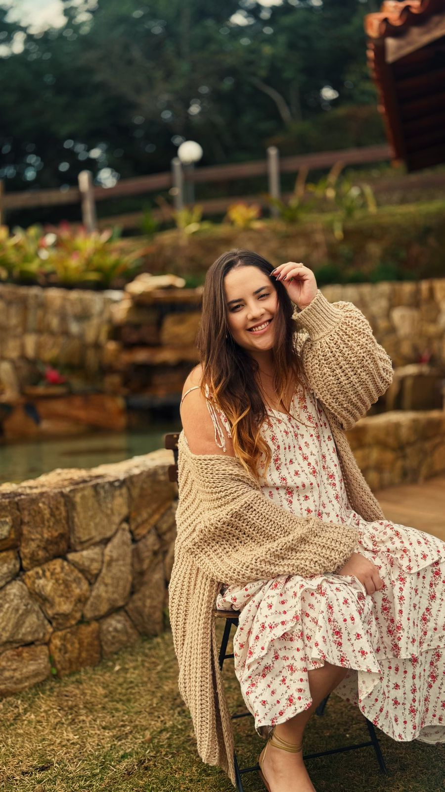 Lara Vasconcelos sorrindo, sentada em um jardim
